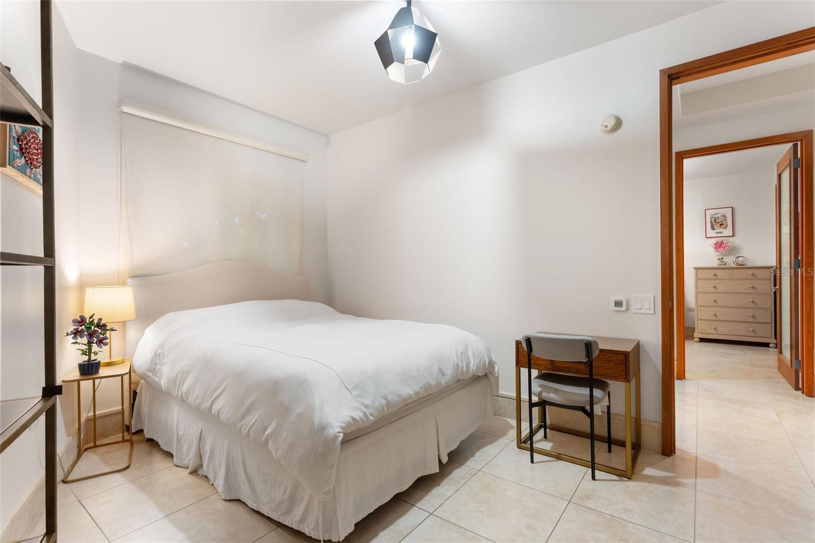 Bedroom with a white bed, tiled floor, and open doorway to a furnished room.