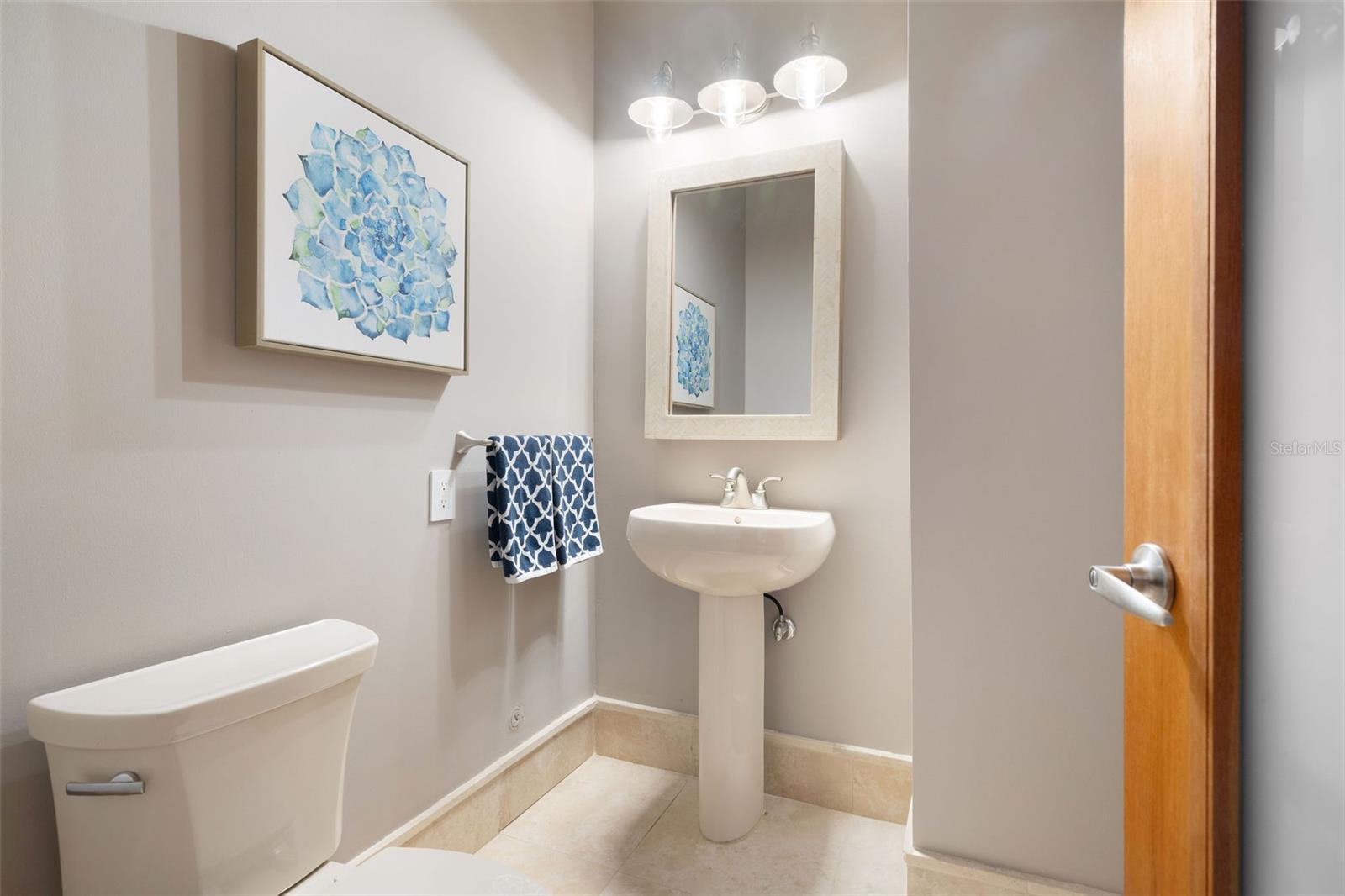 Bathroom with a pedestal sink, framed mirror, blue floral artwork, and patterned hand towels.