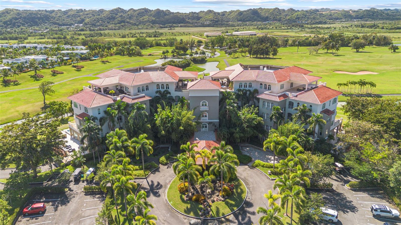 Aerial view of a large residence beside a golf course, palms, and green hills.