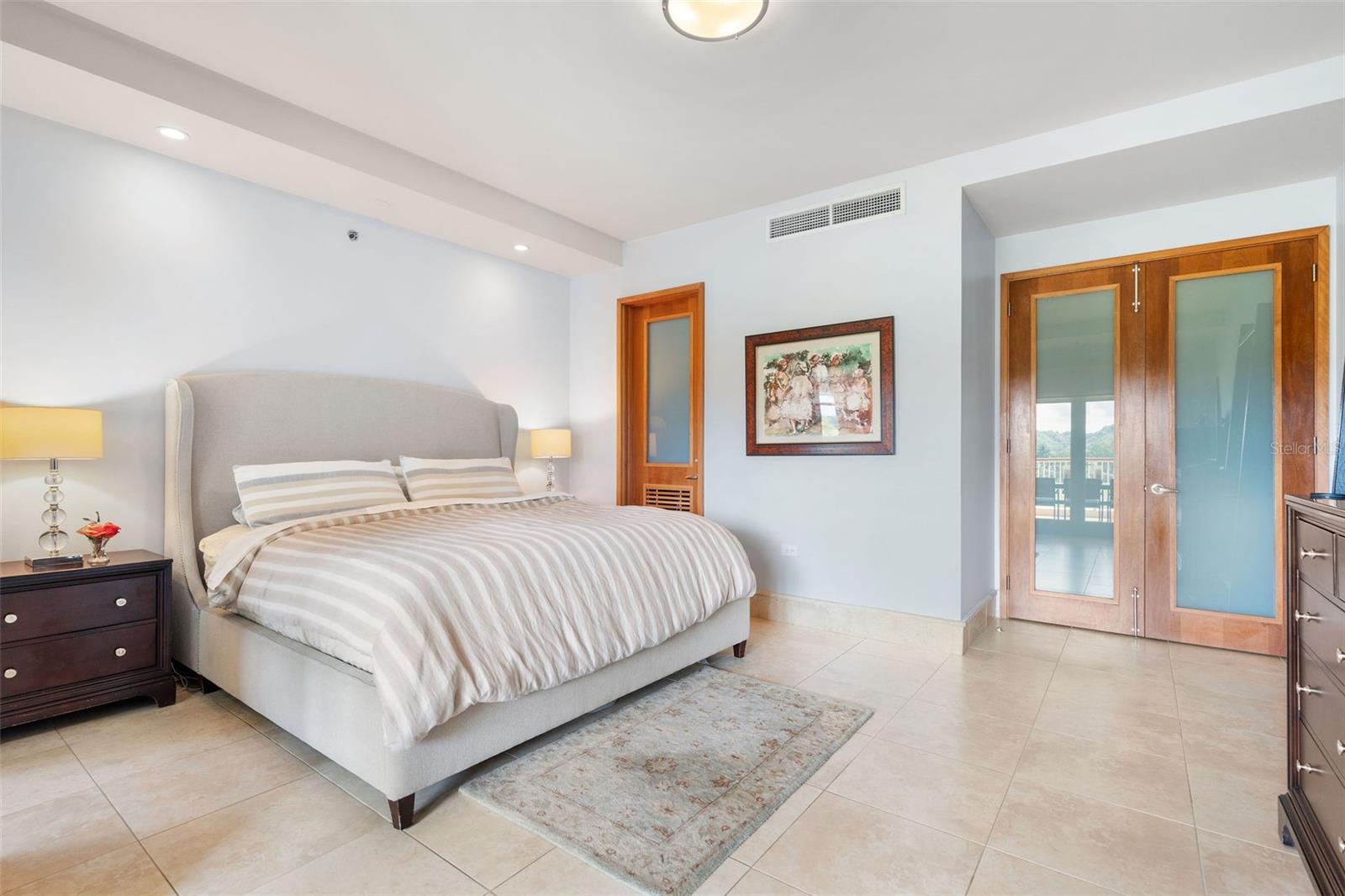 Bedroom with a large upholstered bed, striped bedding, and wooden glass-panel doors.