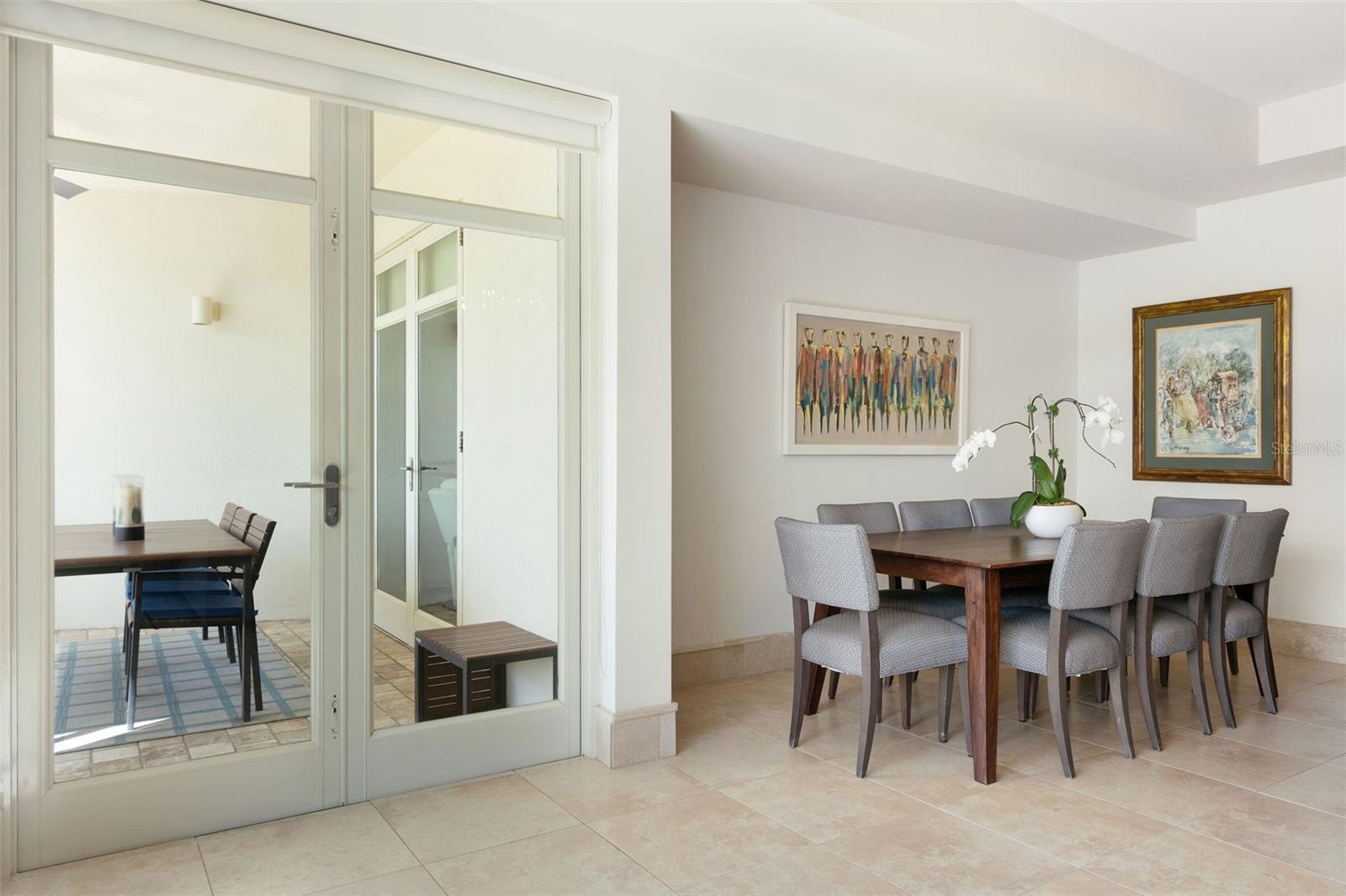 Dining room with a dark wood table, gray chairs, framed artwork, and glass doors to a tiled patio.