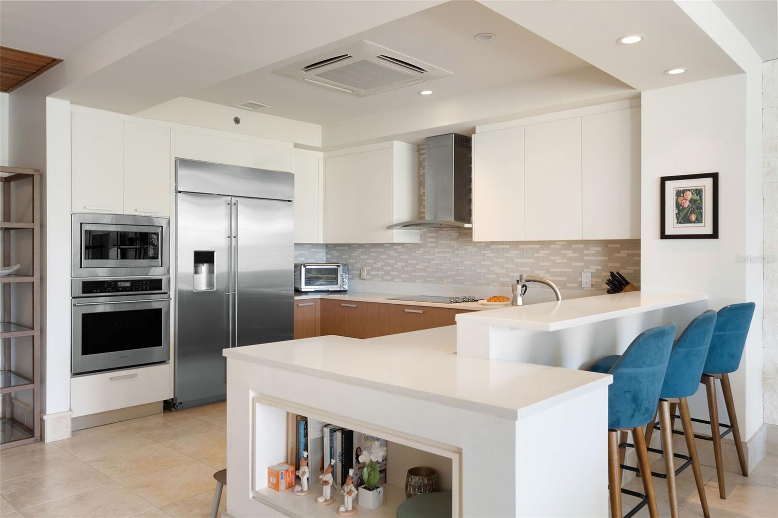 Modern kitchen with stainless steel appliances, a large white island, and blue bar stools.