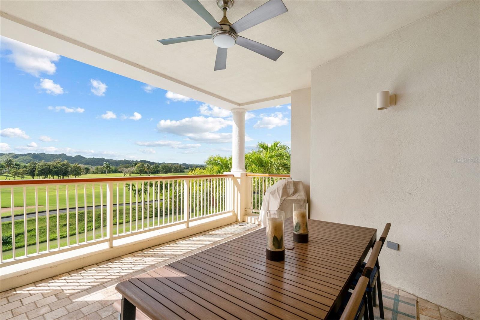 Covered balcony with an outdoor dining table overlooking a green golf course and distant hills.