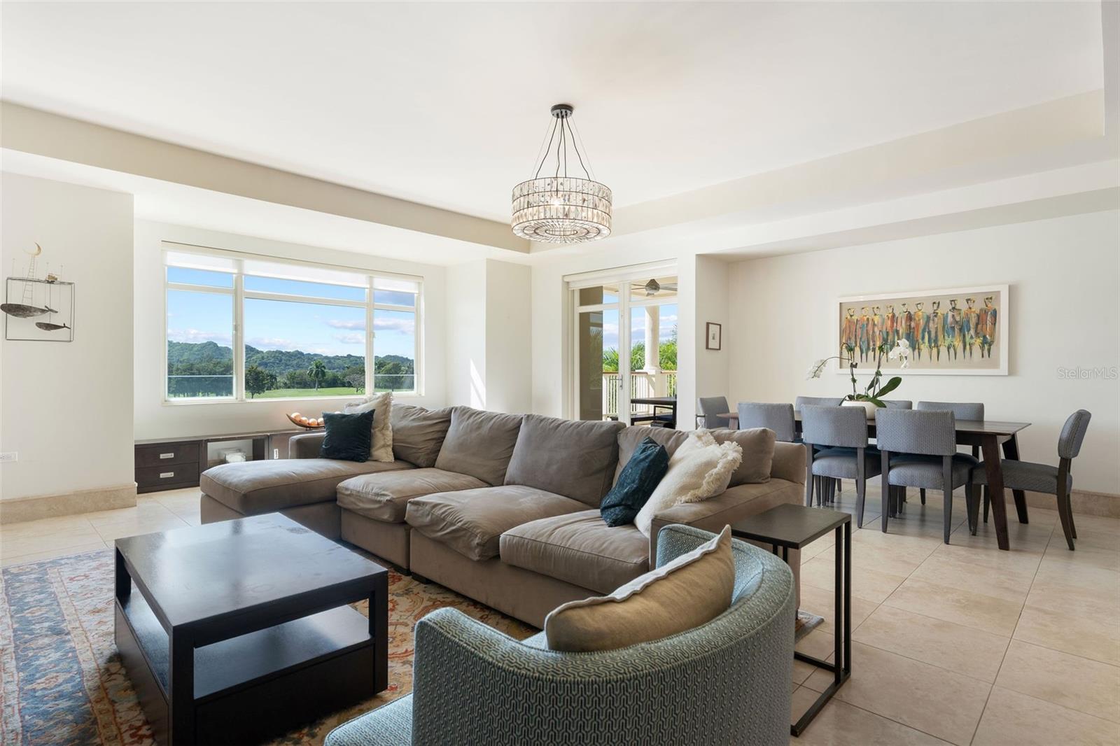 Furnished living and dining room with a gray sectional and large windows overlooking green hills.