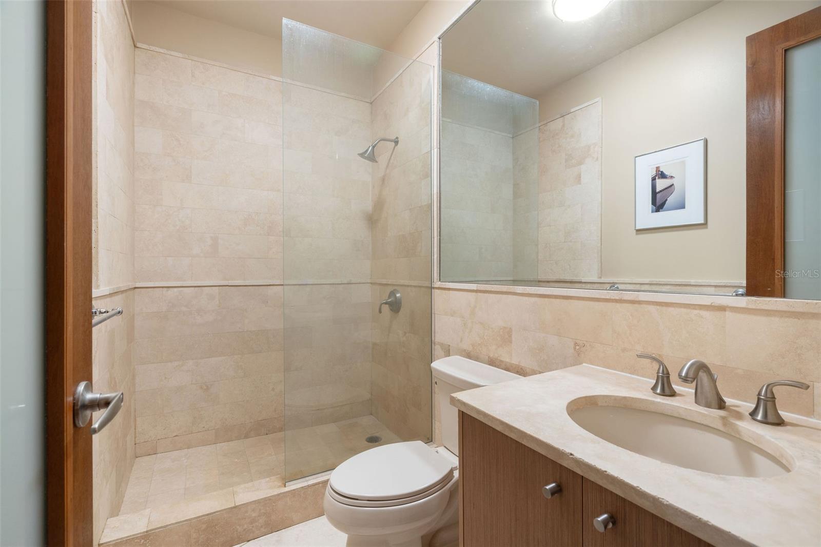 Bathroom with a glass walk-in shower, beige stone tile, and wood vanity.