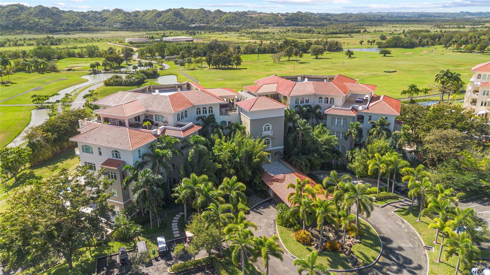 Aerial view of a red-tile-roofed residential complex beside golf course fairways and ponds.
