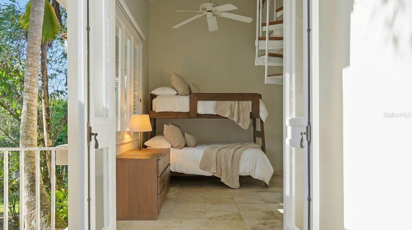 Bedroom with a wooden bunk bed and open doors overlooking palm trees.