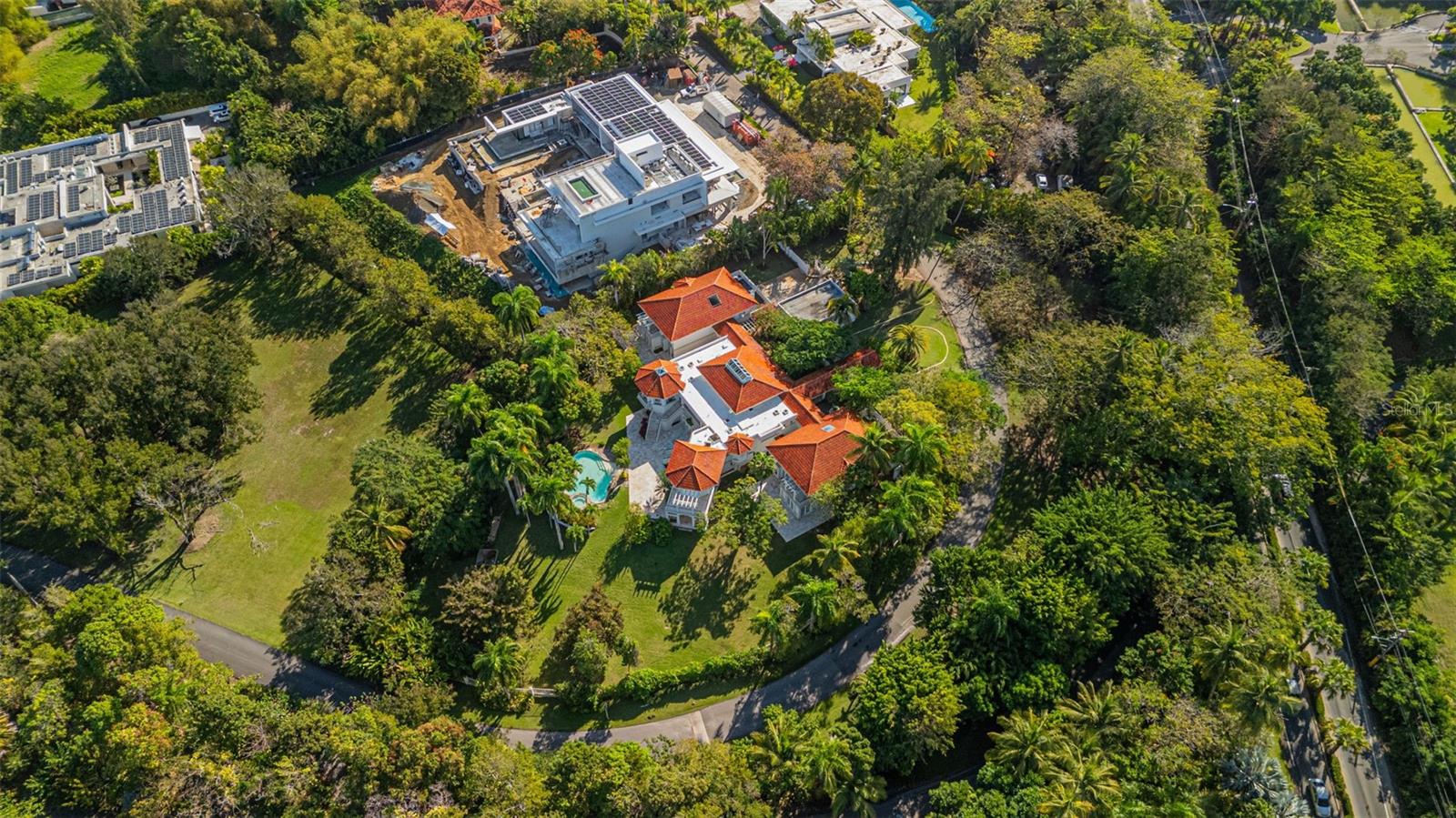 Aerial view of a red tile-roof estate, swimming pool, and spacious lawn amid tropical trees.
