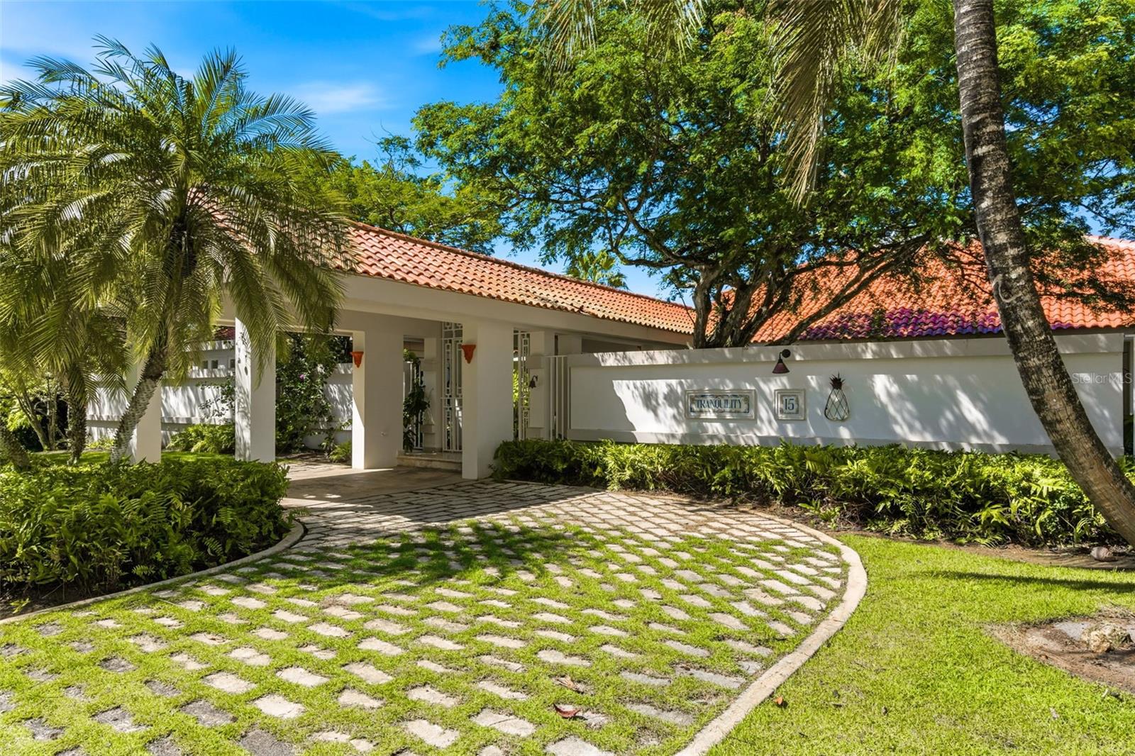 Home entrance with red tile roof, tropical landscaping, and curved stone-and-grass driveway.