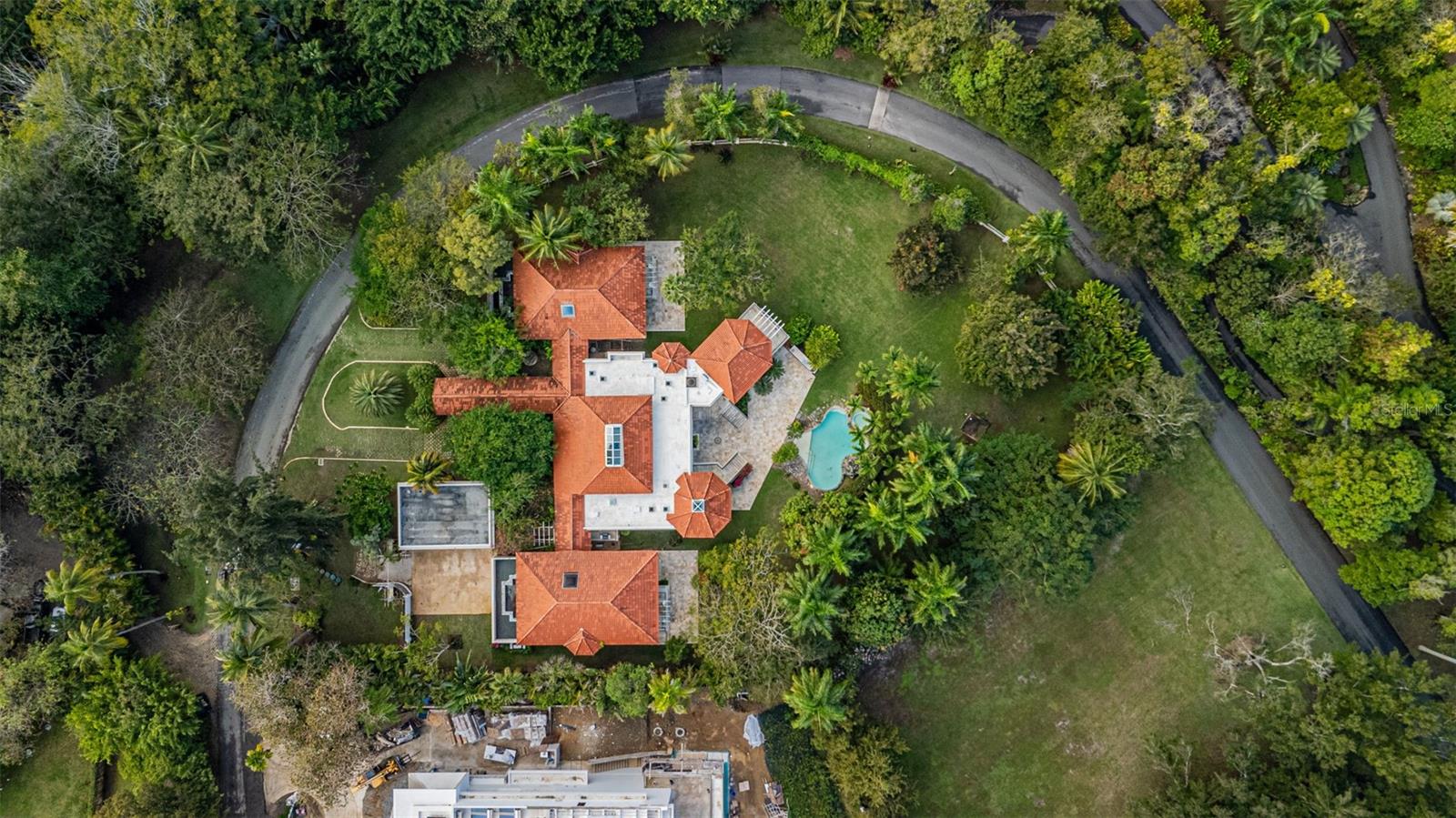 Aerial view of a terracotta-roofed home with a pool and tropical landscaping.