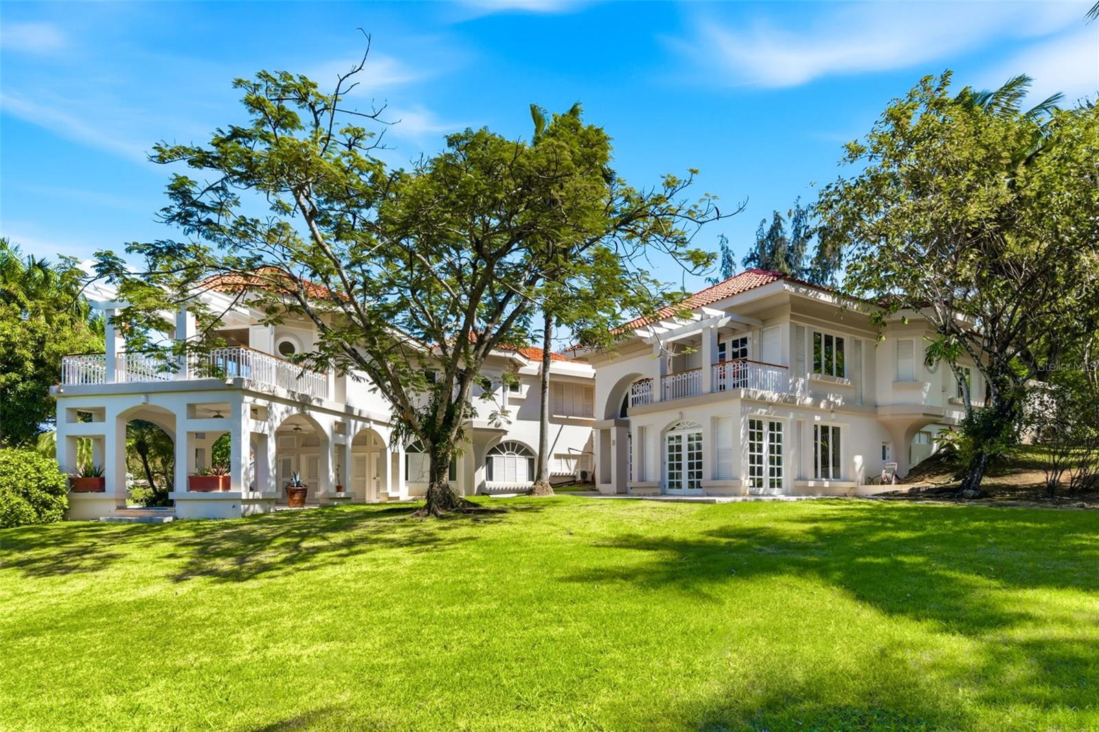 White two-story home with red tile roofs, balconies, arched openings, and a broad lawn.