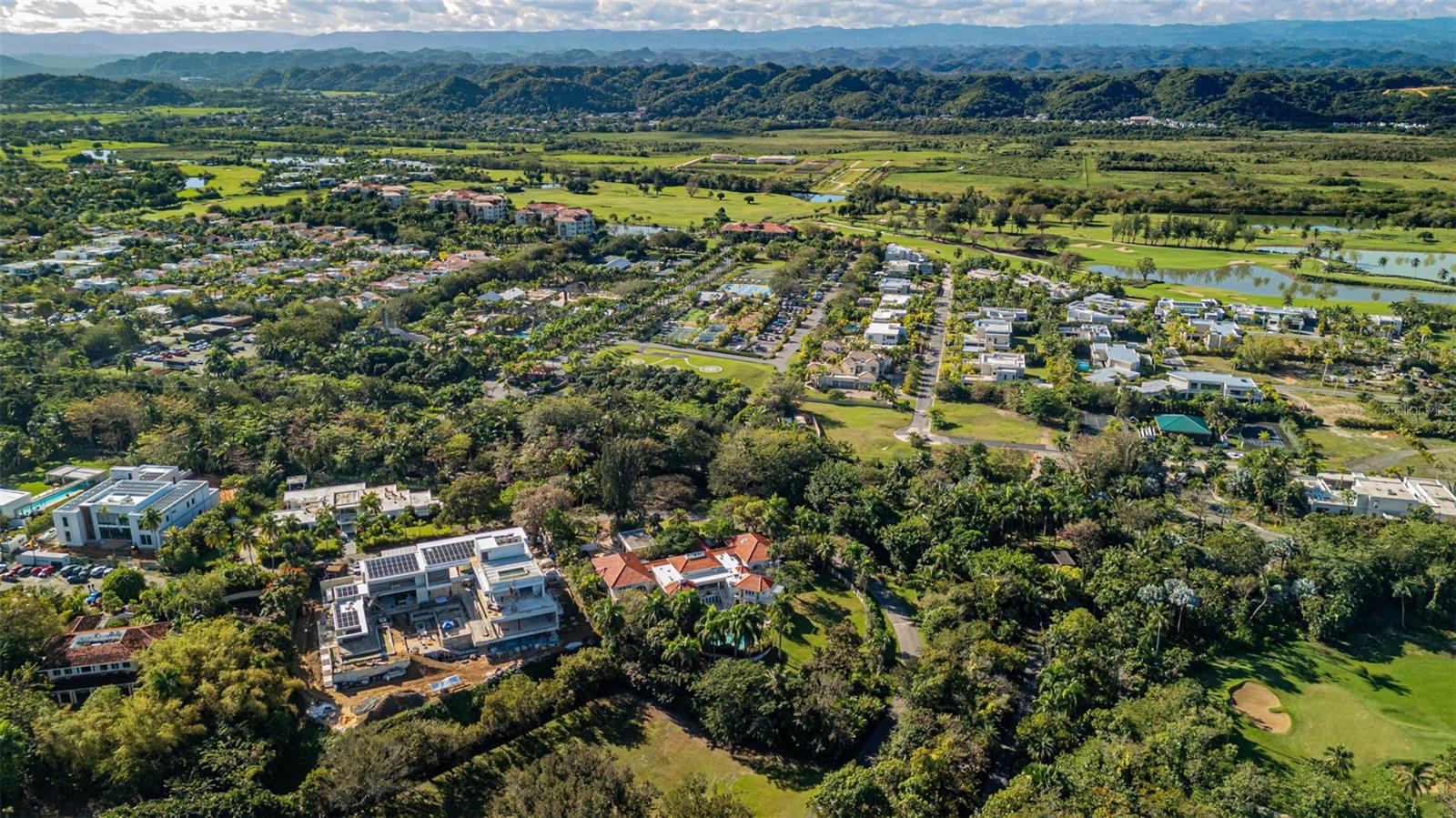Aerial view of homes and golf-course greenery with mountains in the distance.