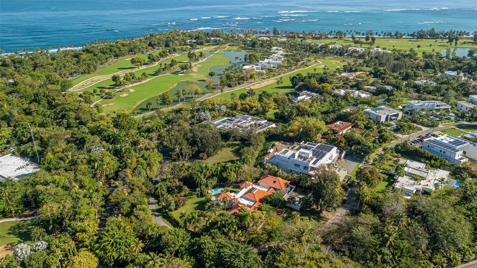 Coastal homes and golf course beside the ocean, viewed from above.