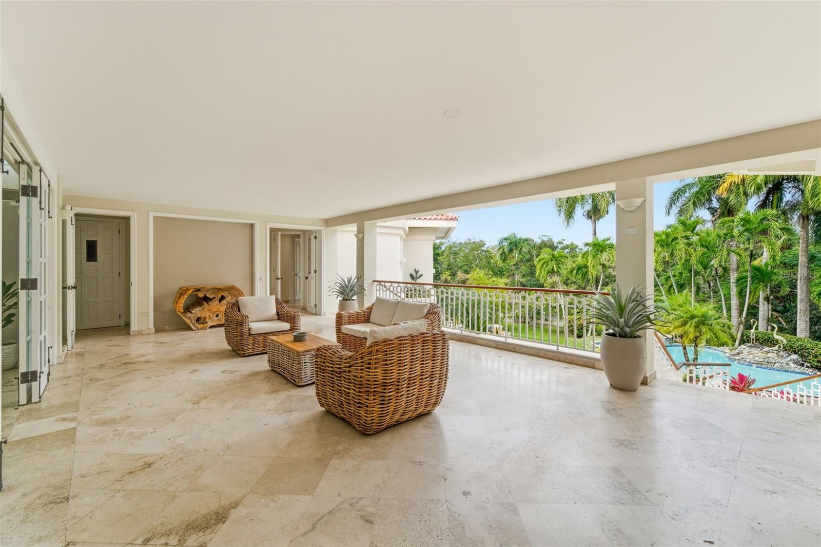 Covered terrace with wicker seating overlooks a swimming pool and tropical palms.