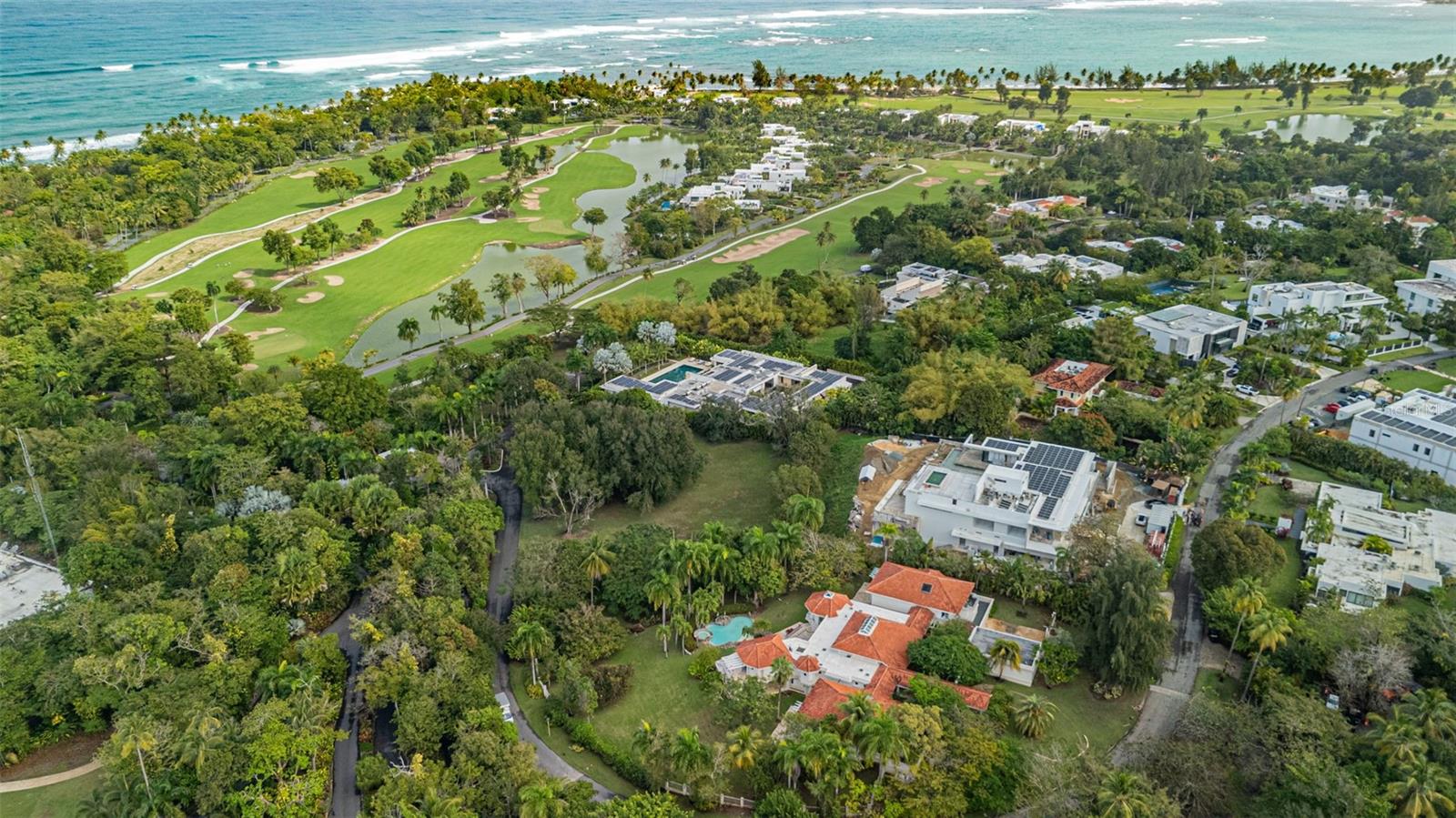 Aerial view of homes beside a golf course and ocean, surrounded by tropical greenery.