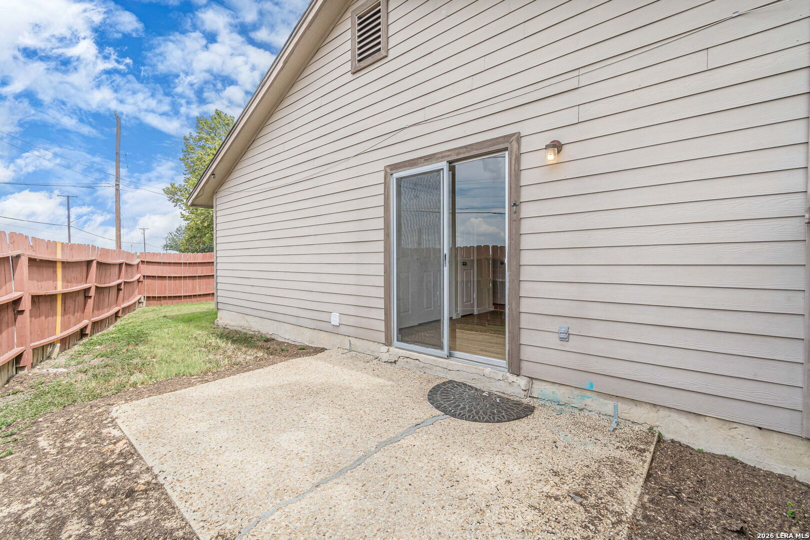 House exterior with a sliding glass door opening onto a concrete patio beside a fenced yard.