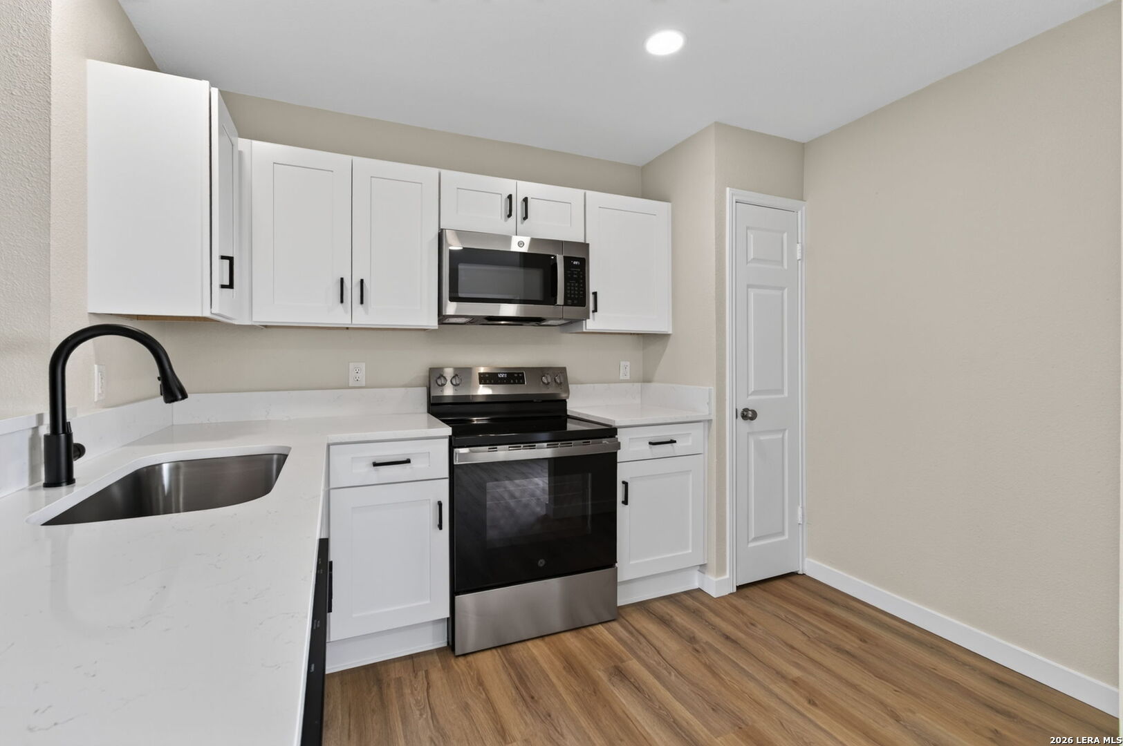Kitchen with white cabinets, stainless steel appliances, white counters, and wood-look flooring.