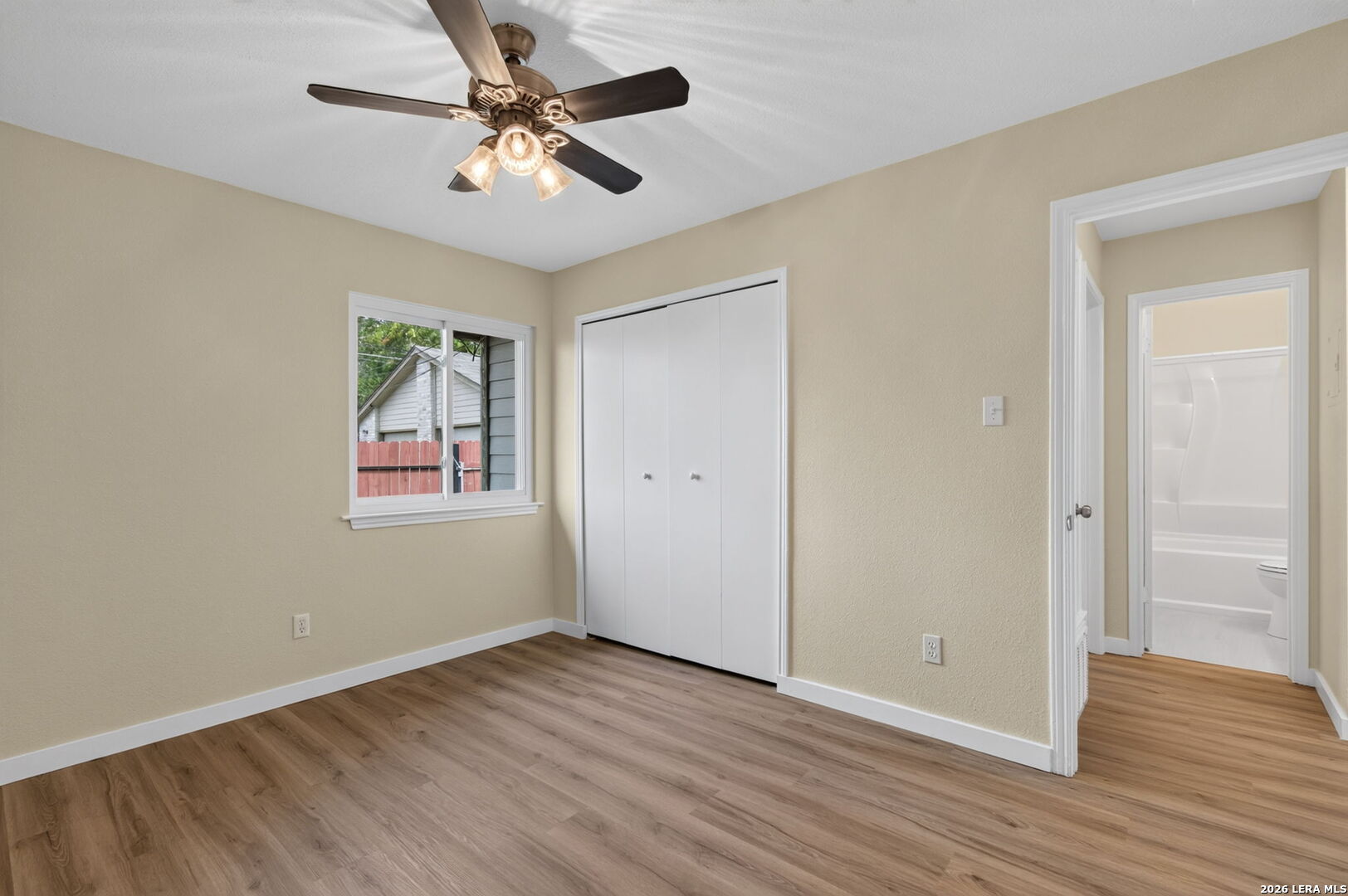 Vacant bedroom with wood-look flooring, a ceiling fan, and a doorway to the bathroom.