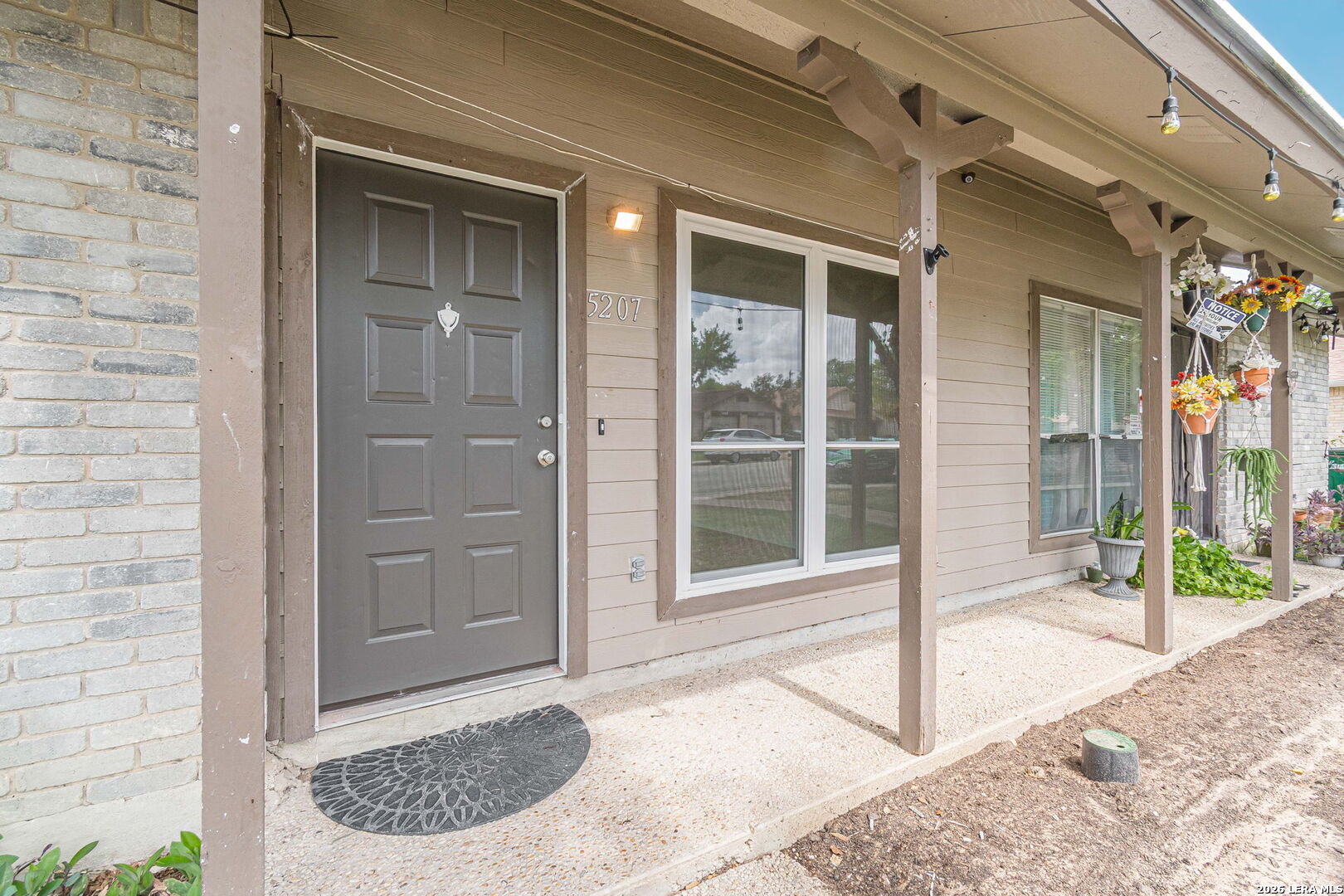 Home entrance with a gray paneled door, covered porch, wide windows, and potted flowers.