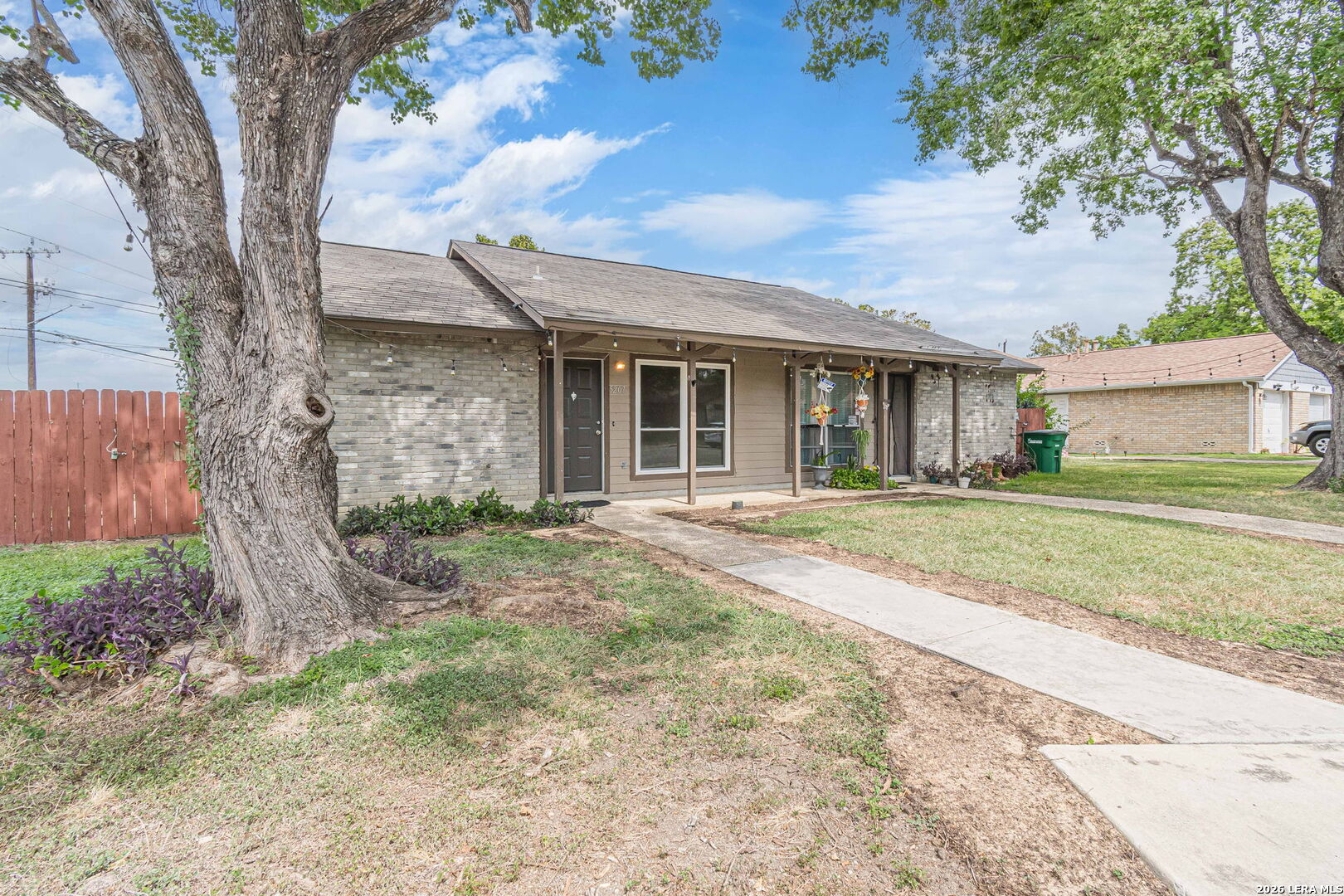 Single-story brick home with a covered entry, mature trees, and a concrete walkway.
