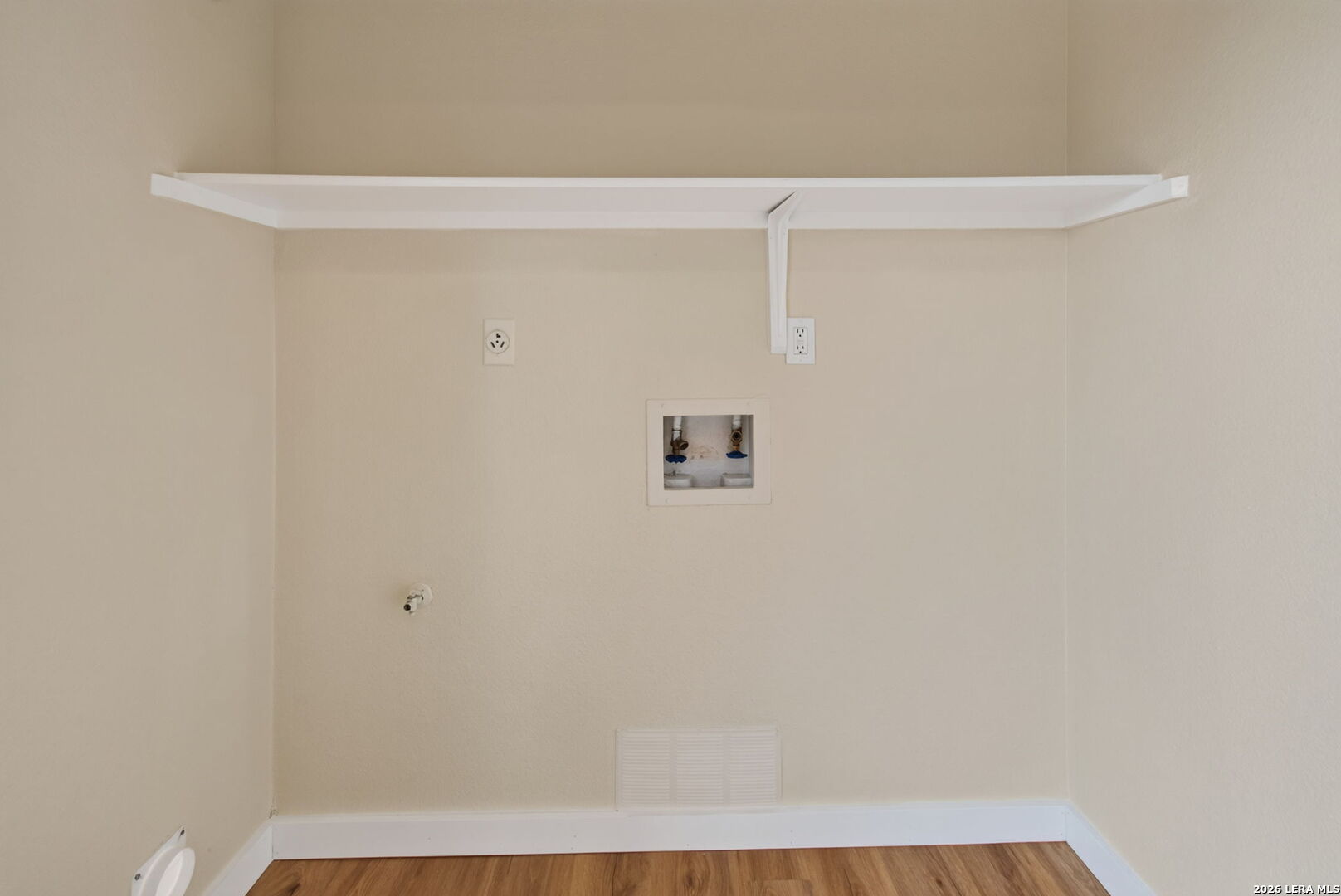 Empty laundry area with washer and dryer hookups beneath a long shelf.