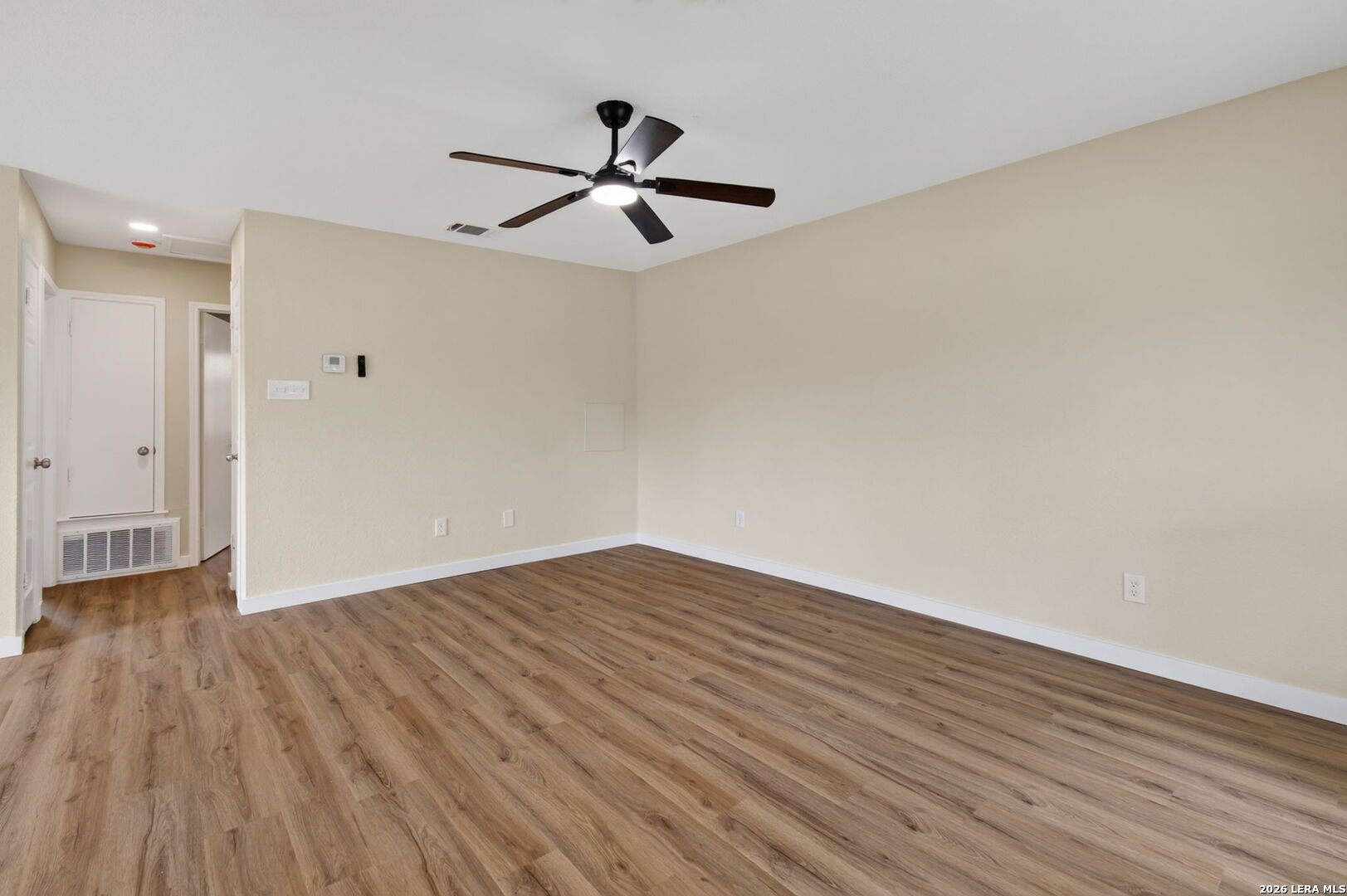 Vacant room with wood-look flooring, beige walls, and a ceiling fan.