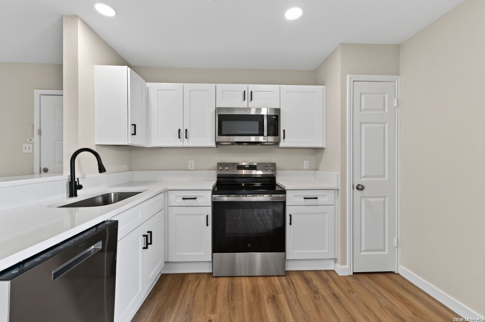 Kitchen with white shaker cabinets, stainless-steel appliances, a black faucet, and wood-look flooring.