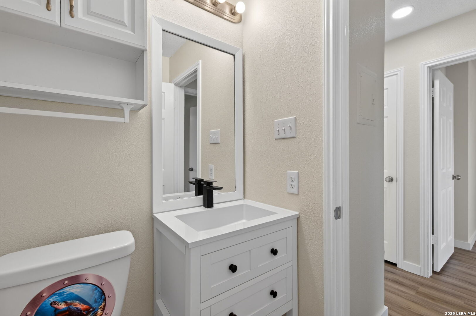 Bathroom with a white vanity, black faucet, large mirror, and colorful ocean-themed toilet seat.