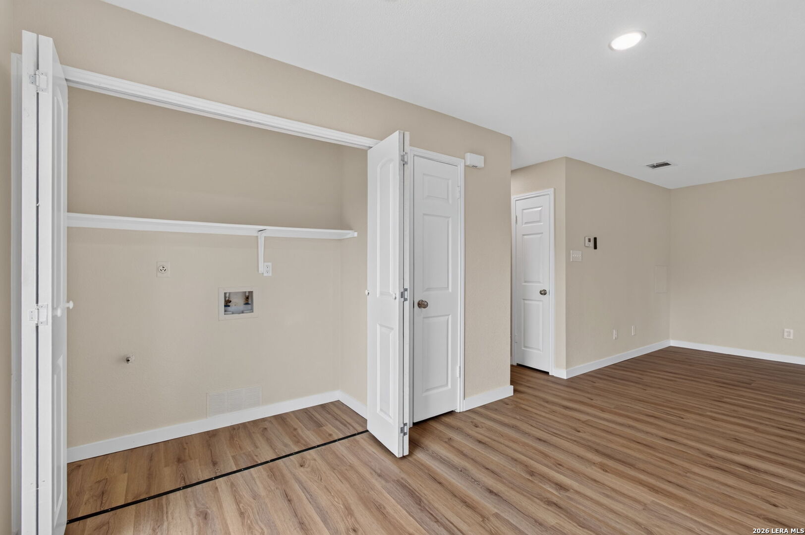 Empty laundry room with washer and dryer hookups, a wall shelf, and wood-look flooring.