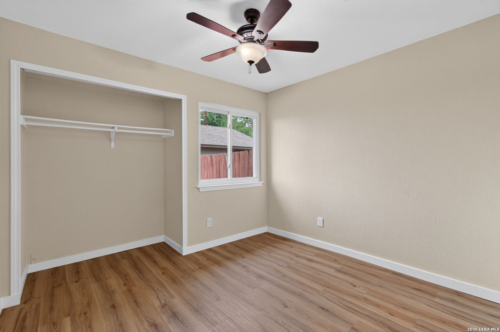 Empty bedroom with a large open closet, wood-look flooring, and a ceiling fan.