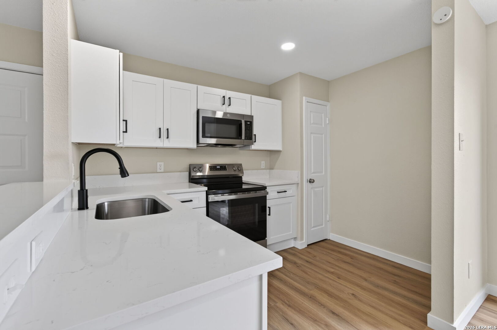 Kitchen with white cabinets, a large peninsula sink, stainless appliances, and wood-look flooring.