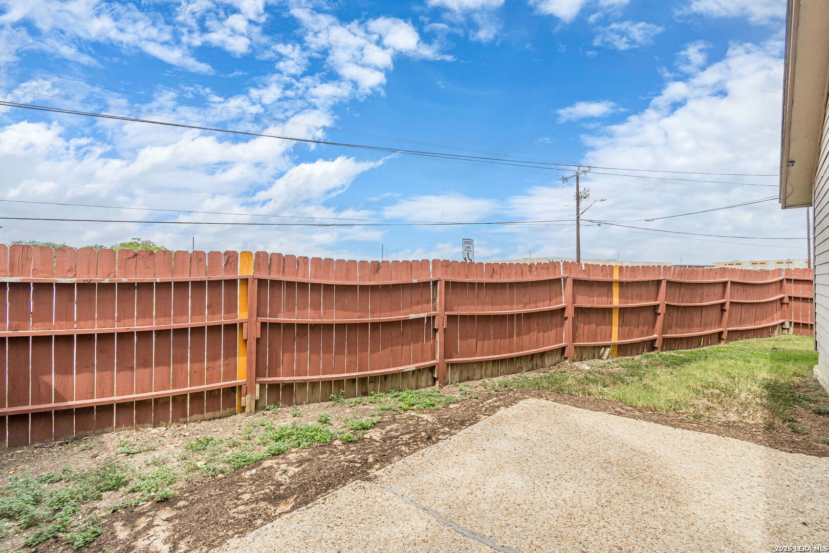 Backyard with a reddish-brown privacy fence, concrete patio, and narrow strip of grass.