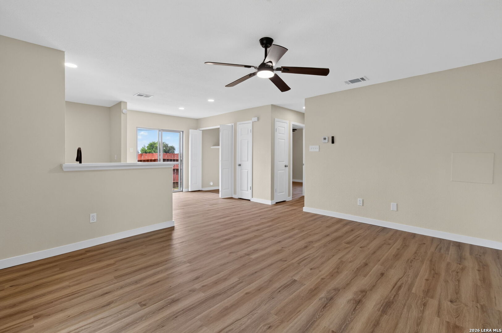 Empty living area with wood-look floors, a ceiling fan, and sliding glass door.
