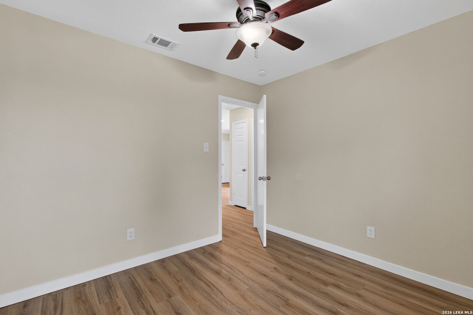 Empty room with wood-look flooring, beige walls, and a ceiling fan with light.