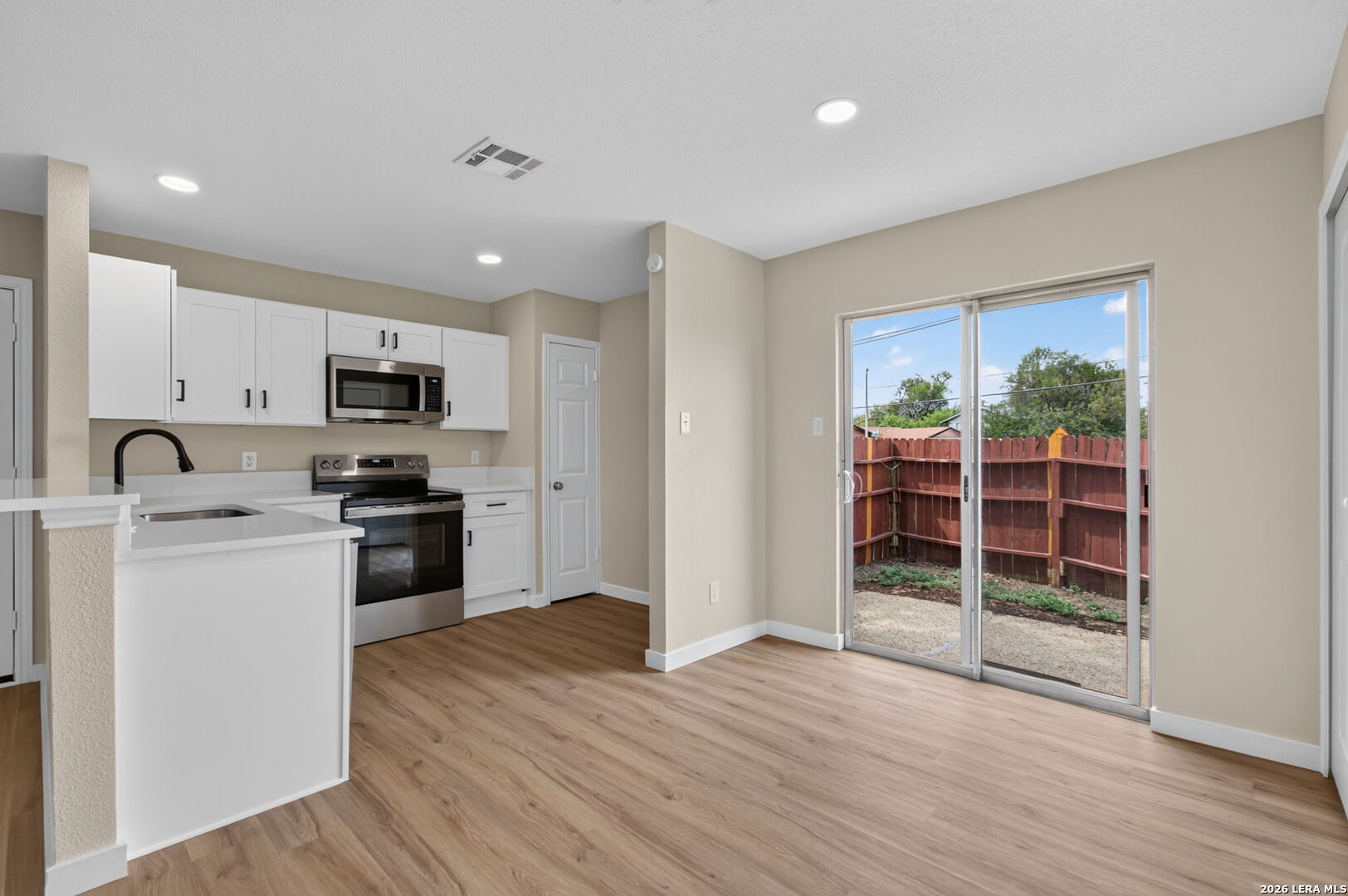 Vacant kitchen with white cabinets, stainless steel appliances, and sliding doors to a fenced backyard.
