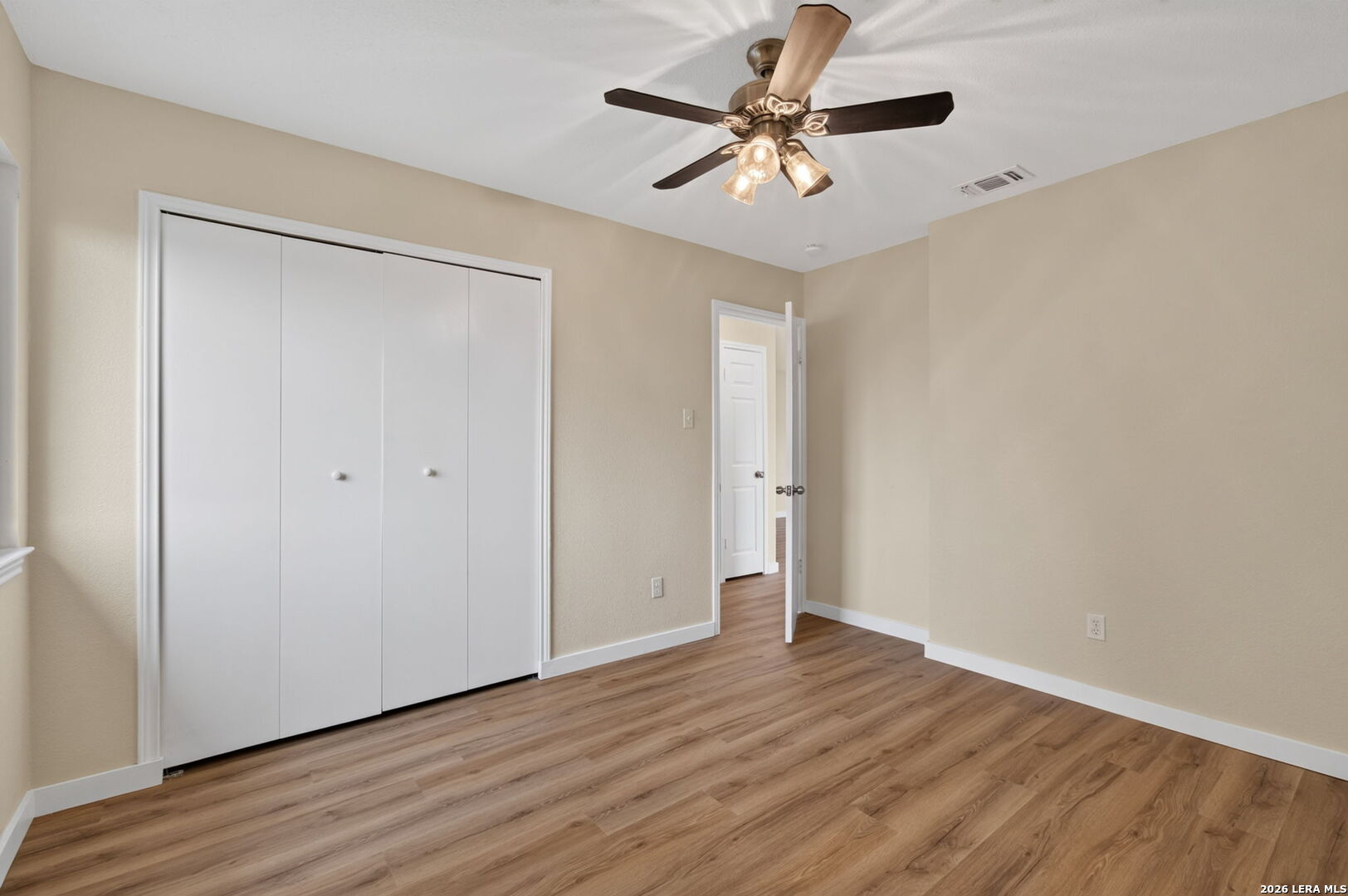 Empty bedroom with sliding closet doors, a ceiling fan, and wood-look flooring.