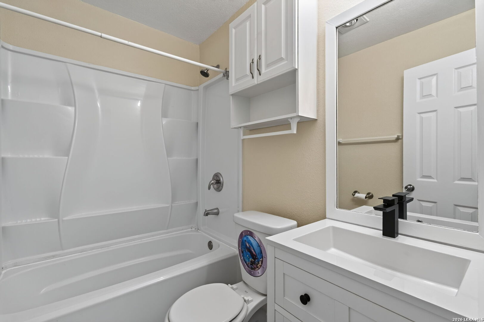 Bathroom with a white tub-shower combination, overhead cabinets, and a vanity with a black faucet.