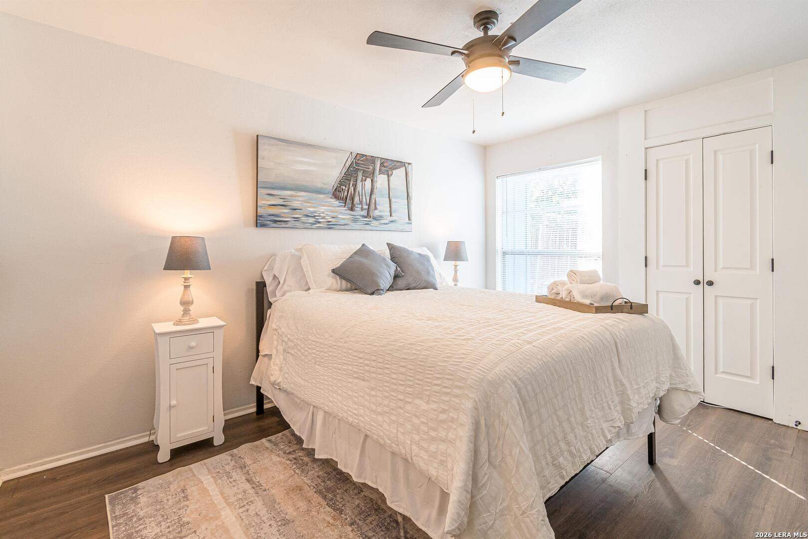 Staged bedroom with a white bed, gray pillows, beach-pier artwork, and a white double-door closet.