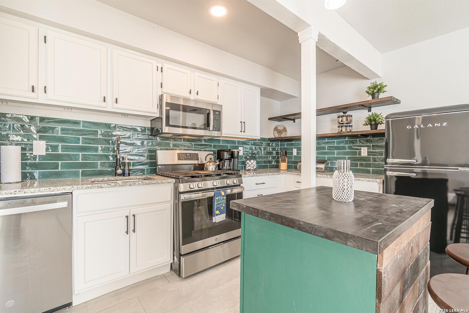 Kitchen with glossy green tile backsplash, white cabinets, and a turquoise island.