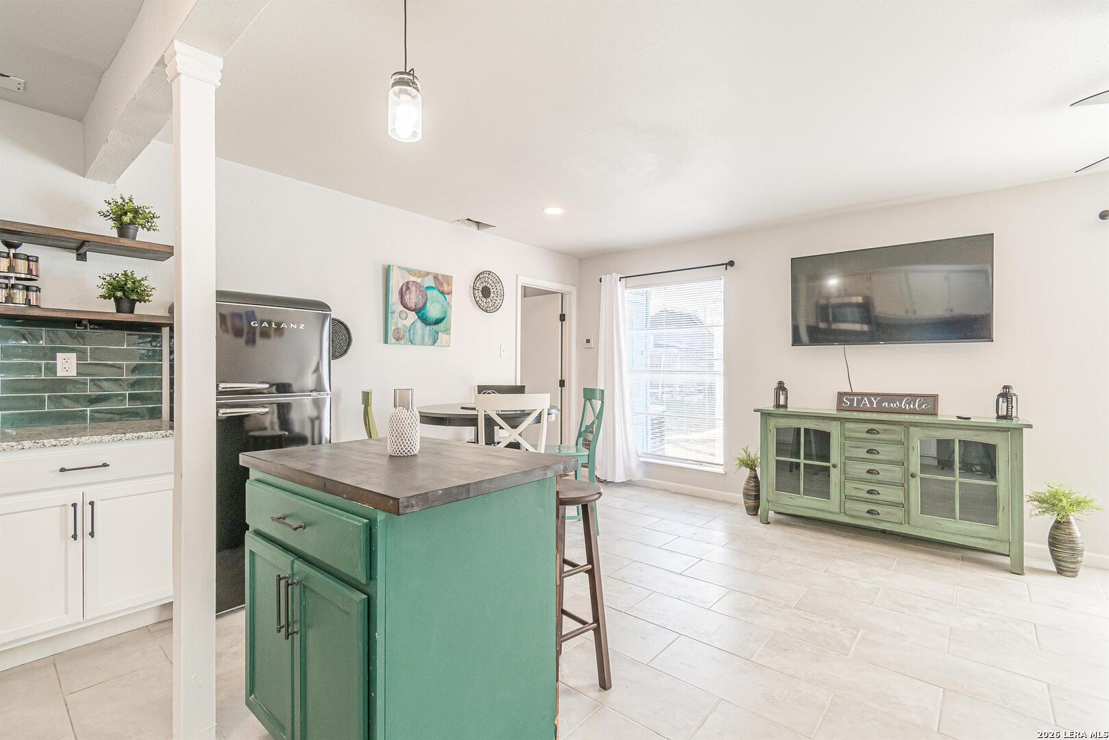 Open-plan kitchen and living area with a teal island, green media cabinet, and wall-mounted television.
