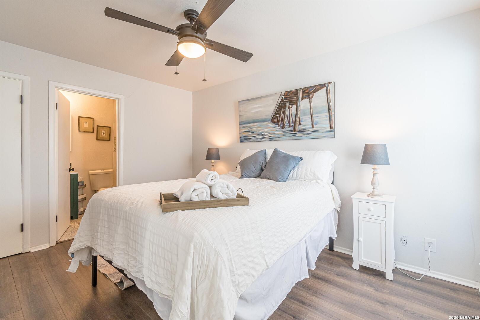 Bedroom with a large white bed, gray pillows, and a ceiling fan.