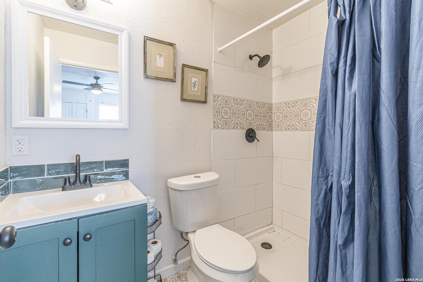 Bathroom with teal vanity, patterned shower tile, and blue curtain.