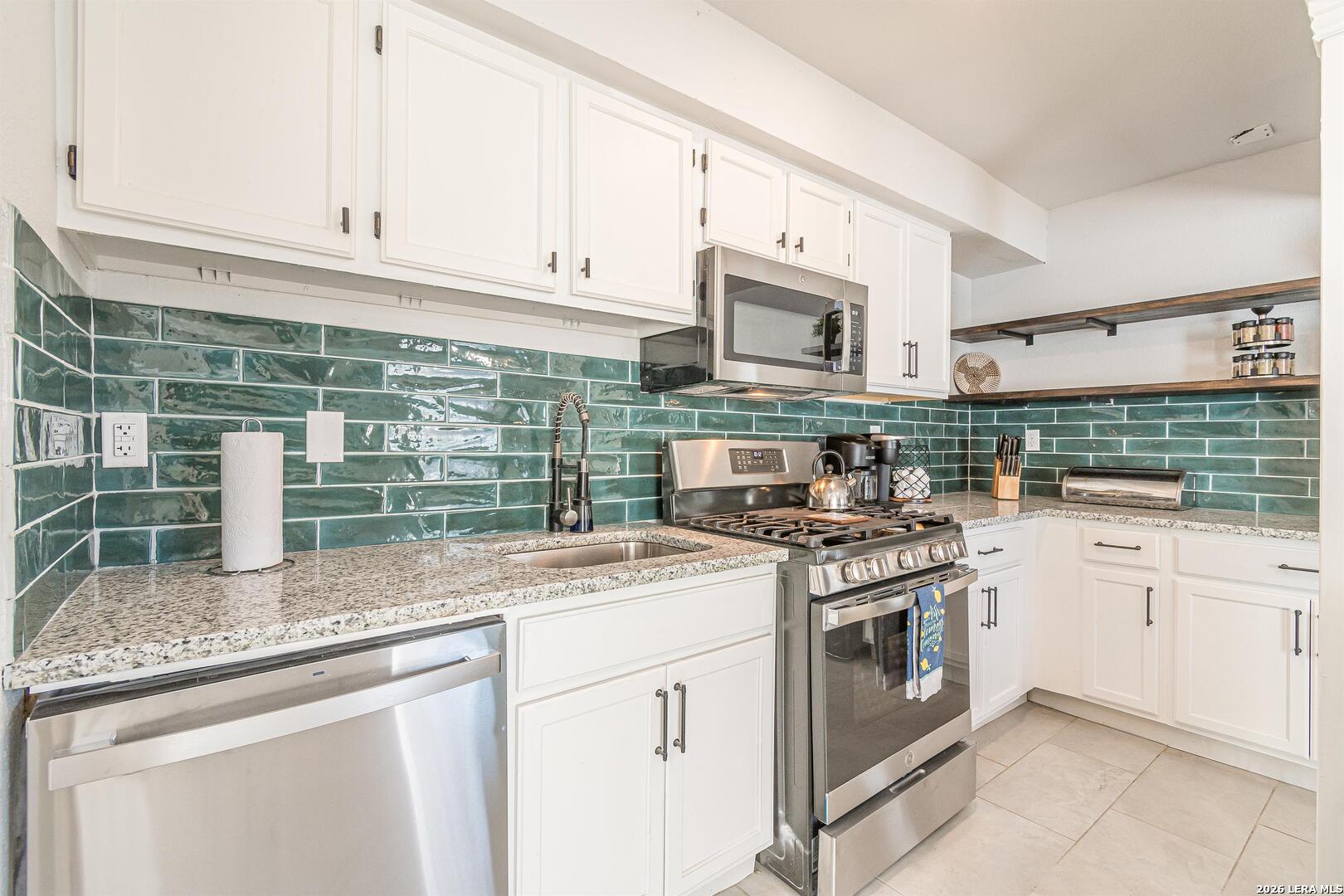 Kitchen with glossy green tile backsplash, white cabinets, and stainless steel appliances.