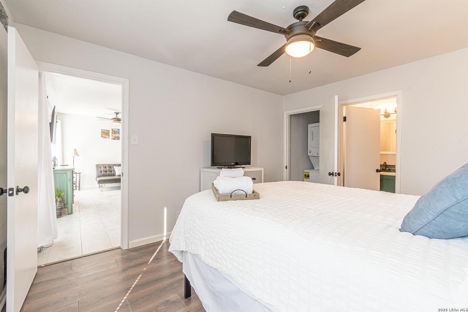 Bedroom with a white bed and ceiling fan, with open doors to laundry and bathroom areas.