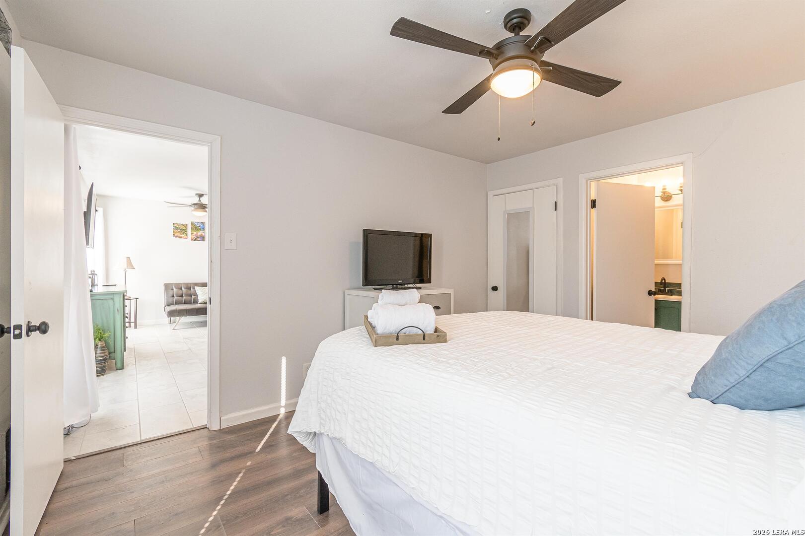 Bedroom with a white-covered bed, ceiling fan, and doorways to the living area and bathroom.