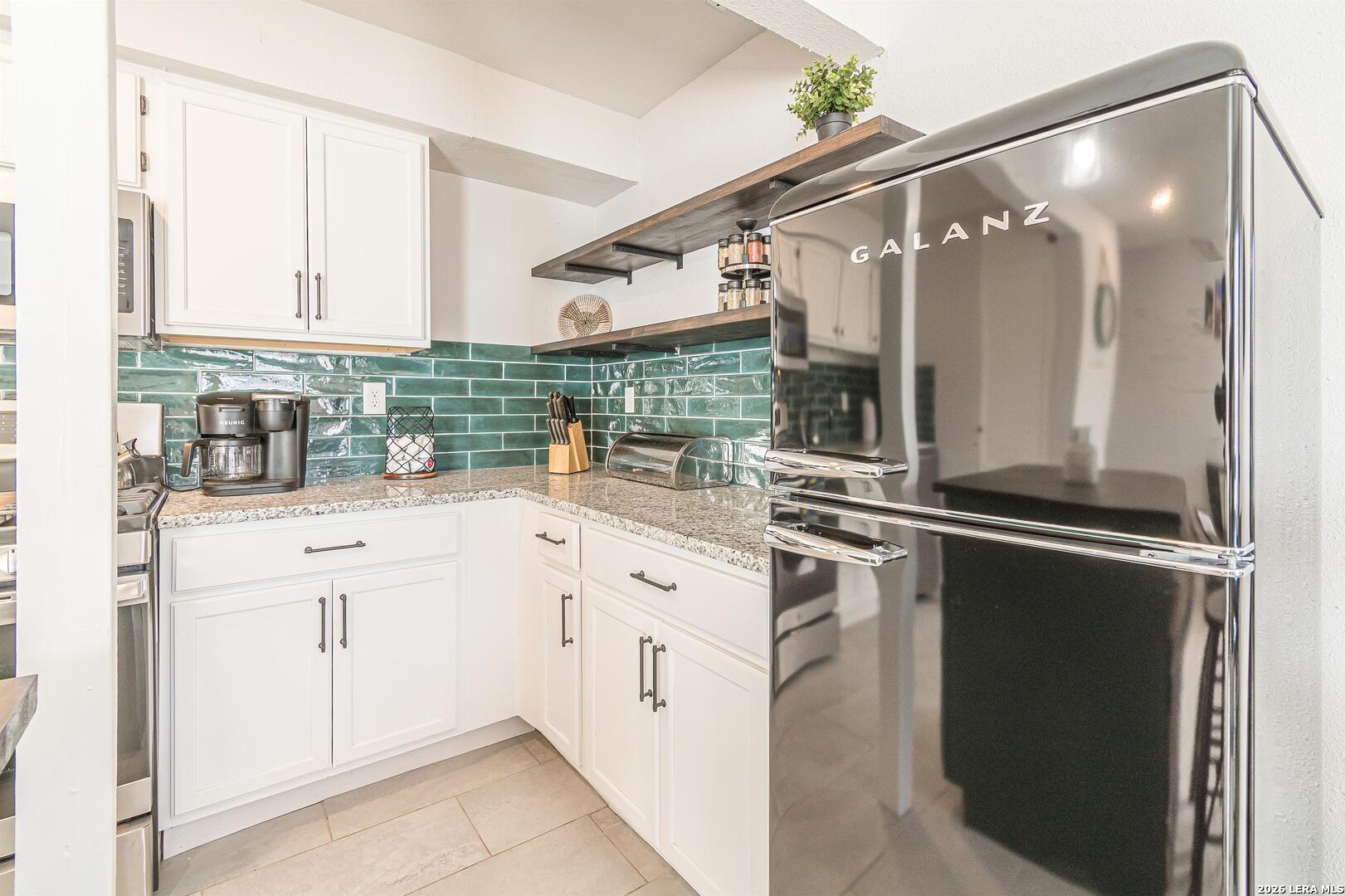 Kitchen with white cabinets, green tile backsplash, granite counters, and a large Galanz refrigerator.