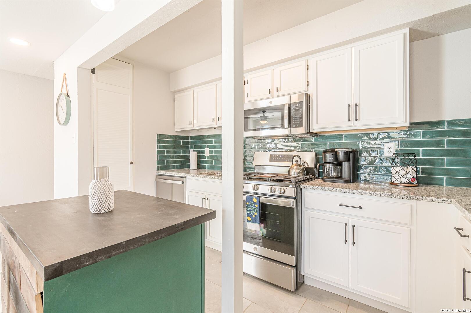 Kitchen with white cabinets, stainless steel appliances, and a glossy teal-green tile backsplash.
