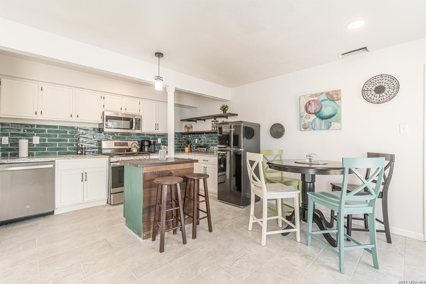 Kitchen and dining area with green tile backsplash, teal island, and colorful chairs.
