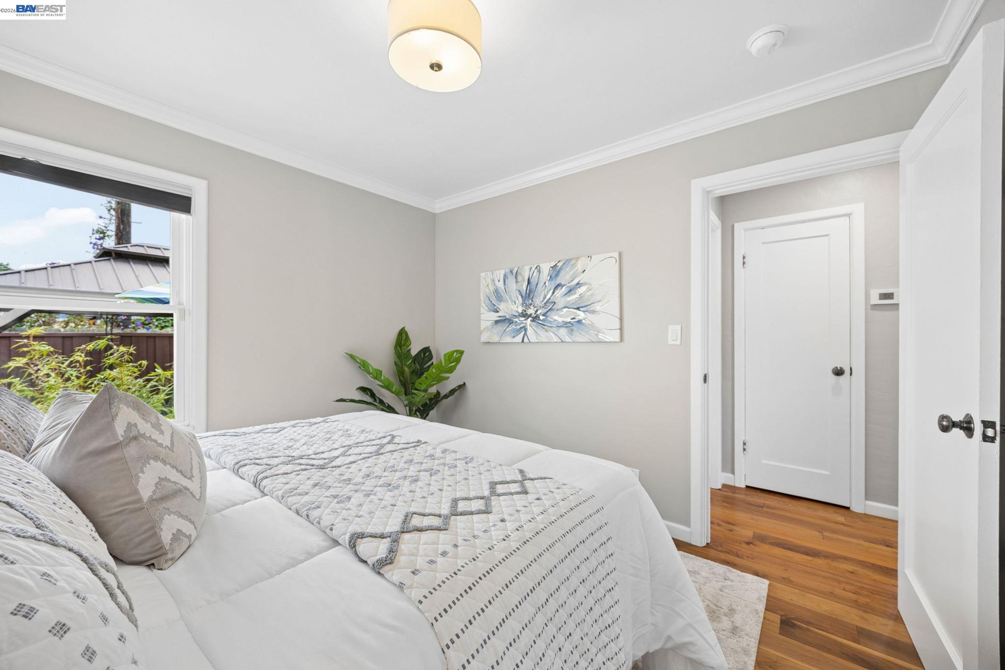 Staged bedroom with a white quilted bed, hardwood floors, and a window overlooking the yard.