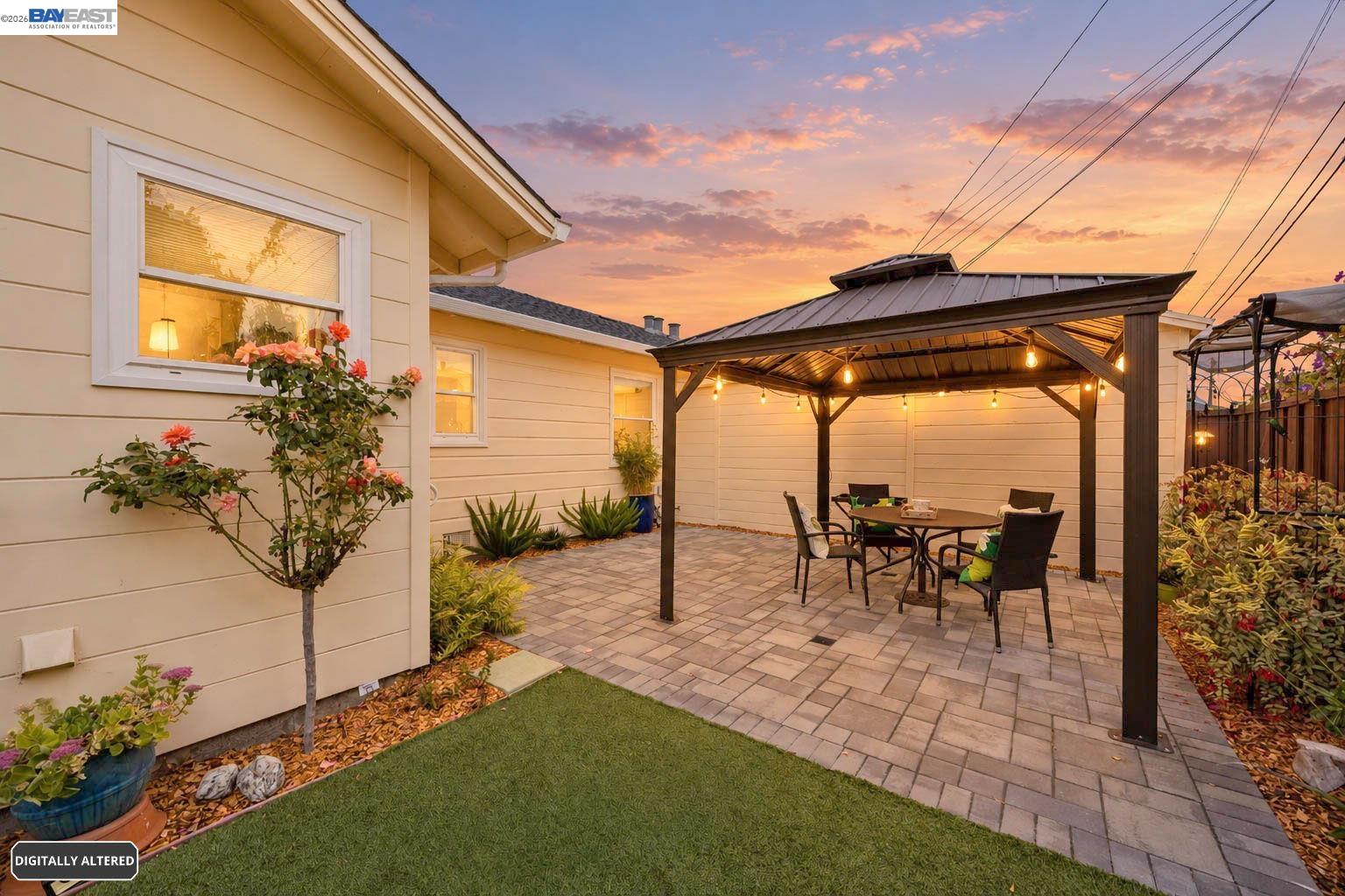 Backyard patio with a lighted pergola, dining set, pavers, and landscaped garden at dusk.